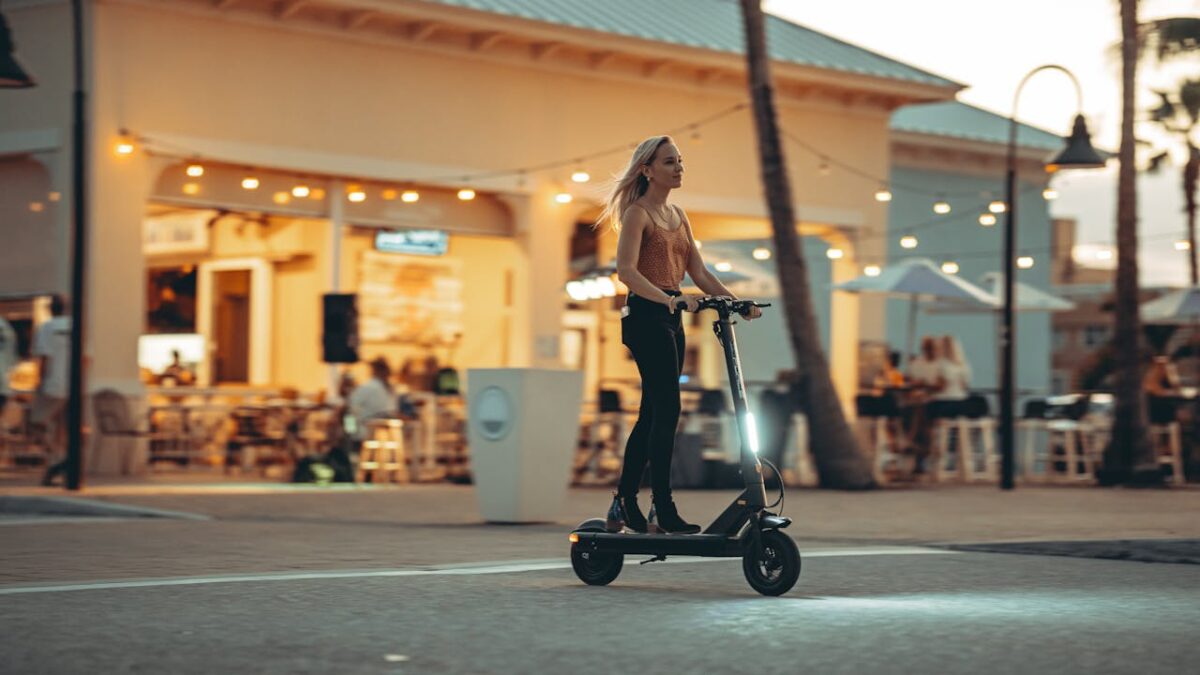 Stylish woman enjoying a ride on an electric scooter in a lively urban area during sunset.
