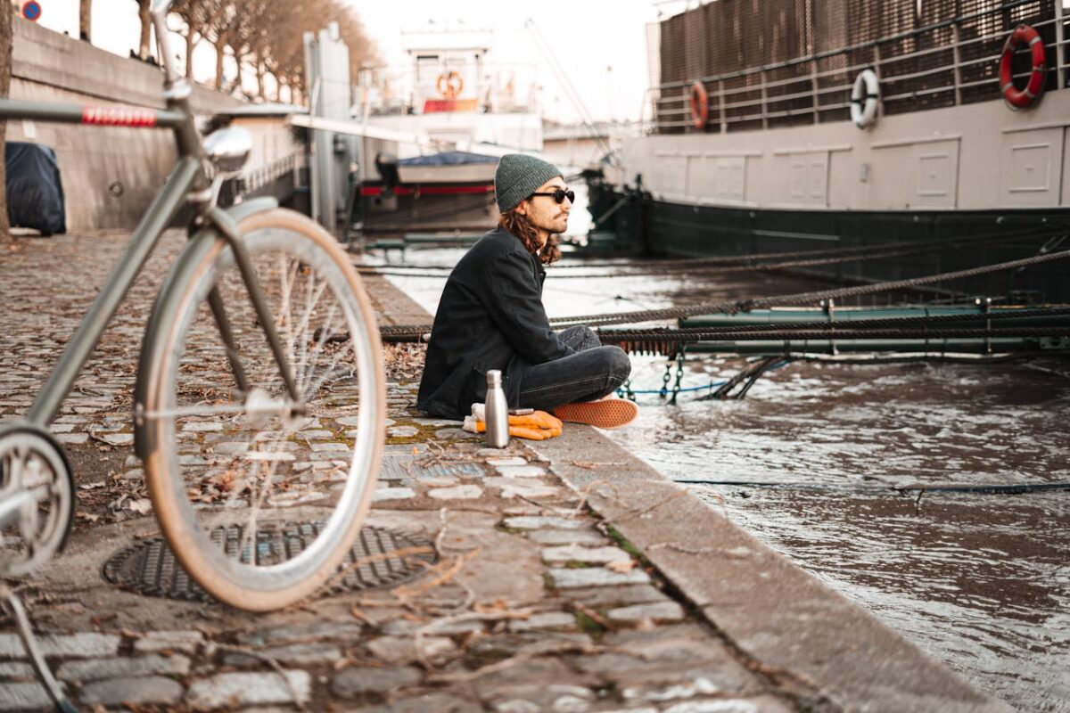 A man sitting by a canal with a bicycle, reflecting urban lifestyle and tranquility.