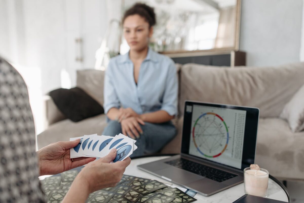 A woman has her fortune read with tarot cards and astrology chart on a laptop.