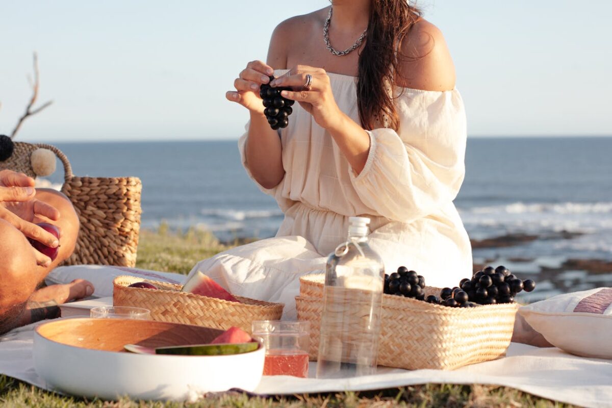 A woman enjoys a serene picnic by the beach with fruits and a woven basket.